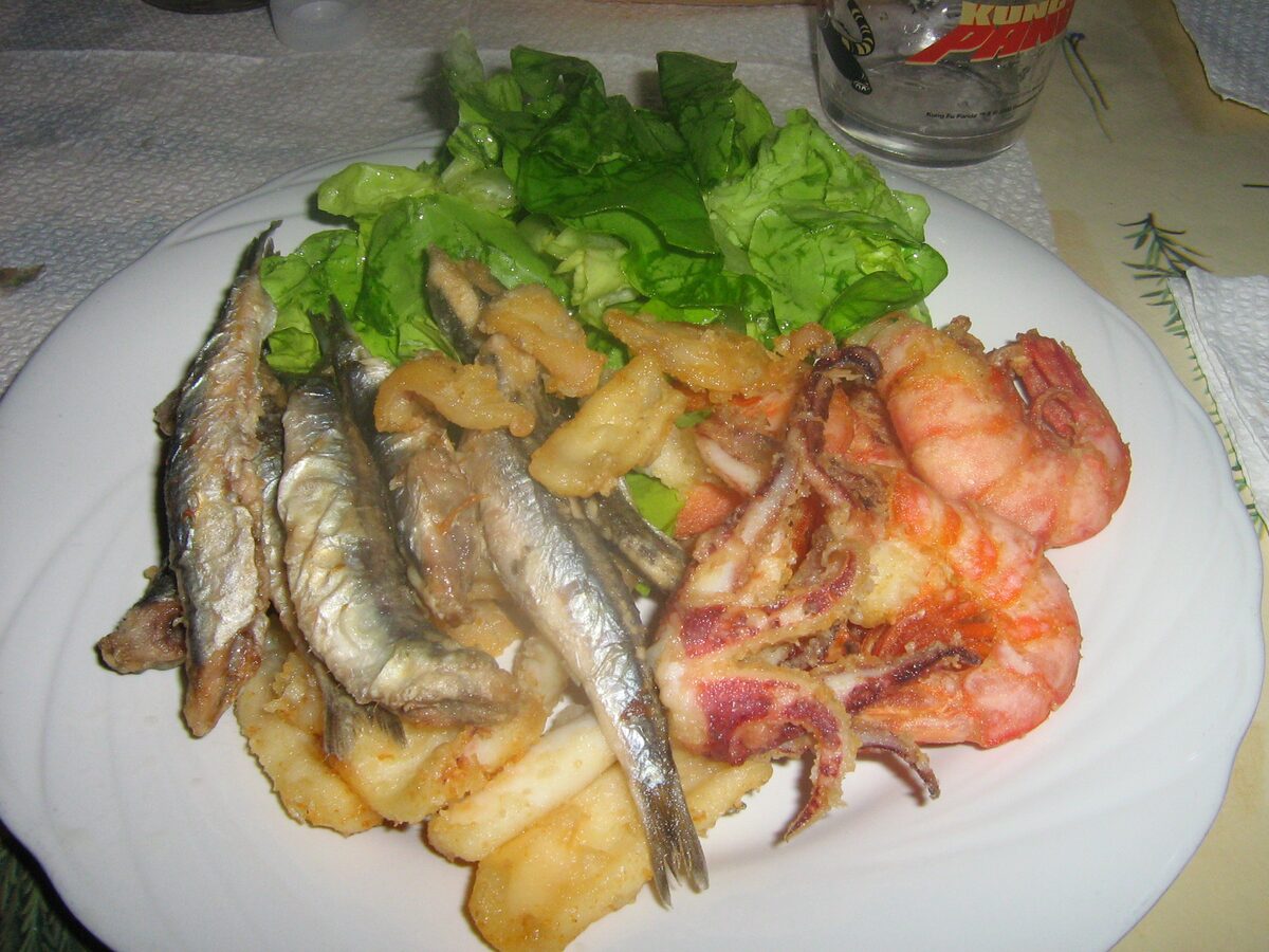 A plate of fried sardines, squid and prawns with salad