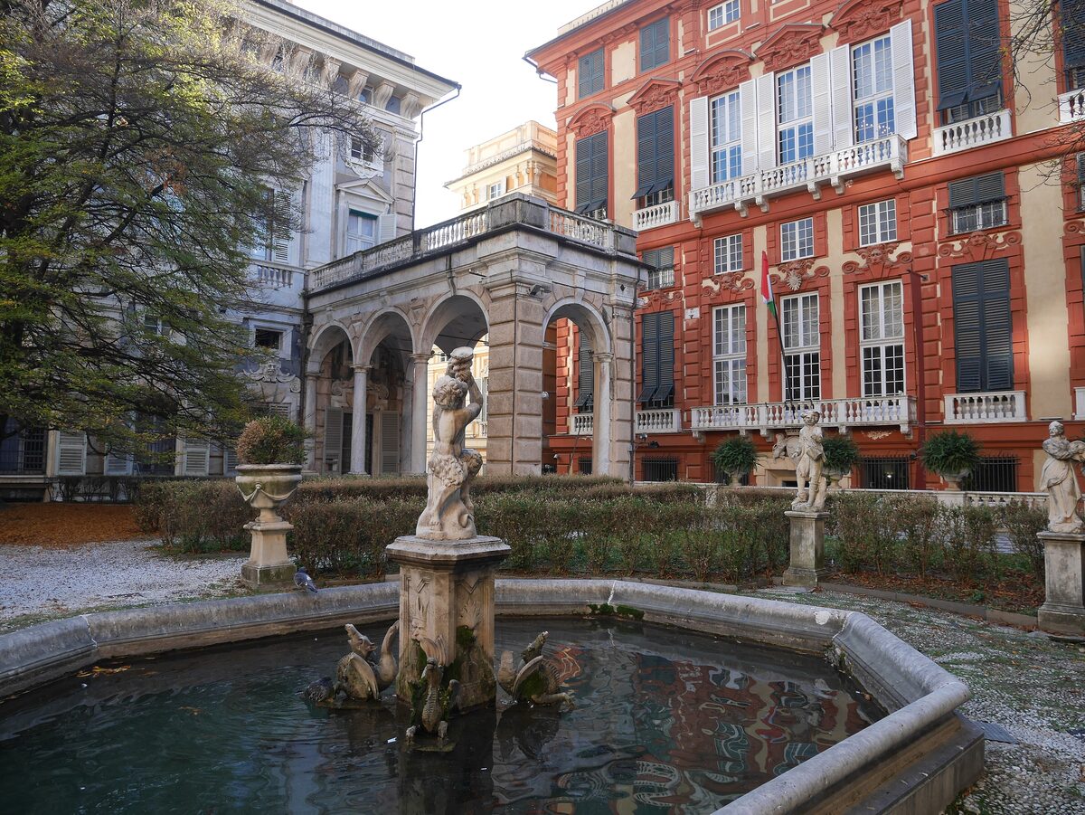The red facade of Palazzo Rosso seen across the garden fountain of Palazzo Bianco