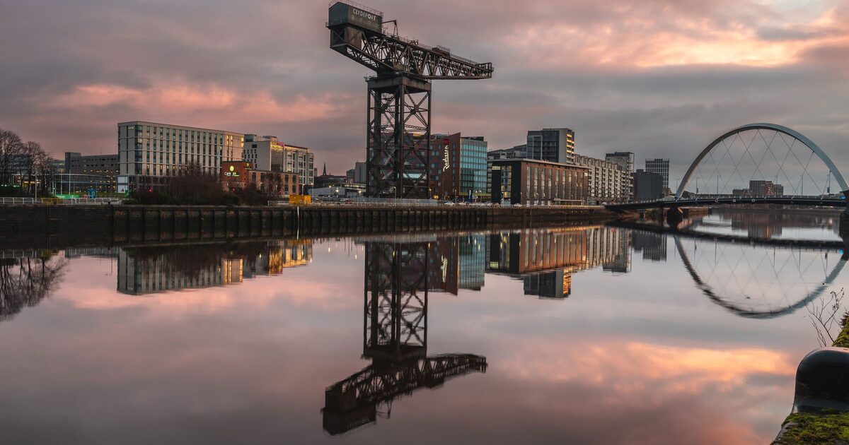 The Finnieston Crane and the arch of the Clyde Arc bridge reflected in the still River Clyde under a pink sunset sky
