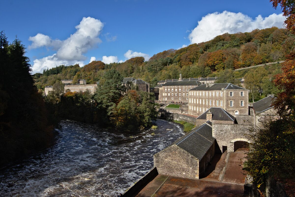 The stone mill buildings of New Lanark beside the River Clyde, in a wooded valley