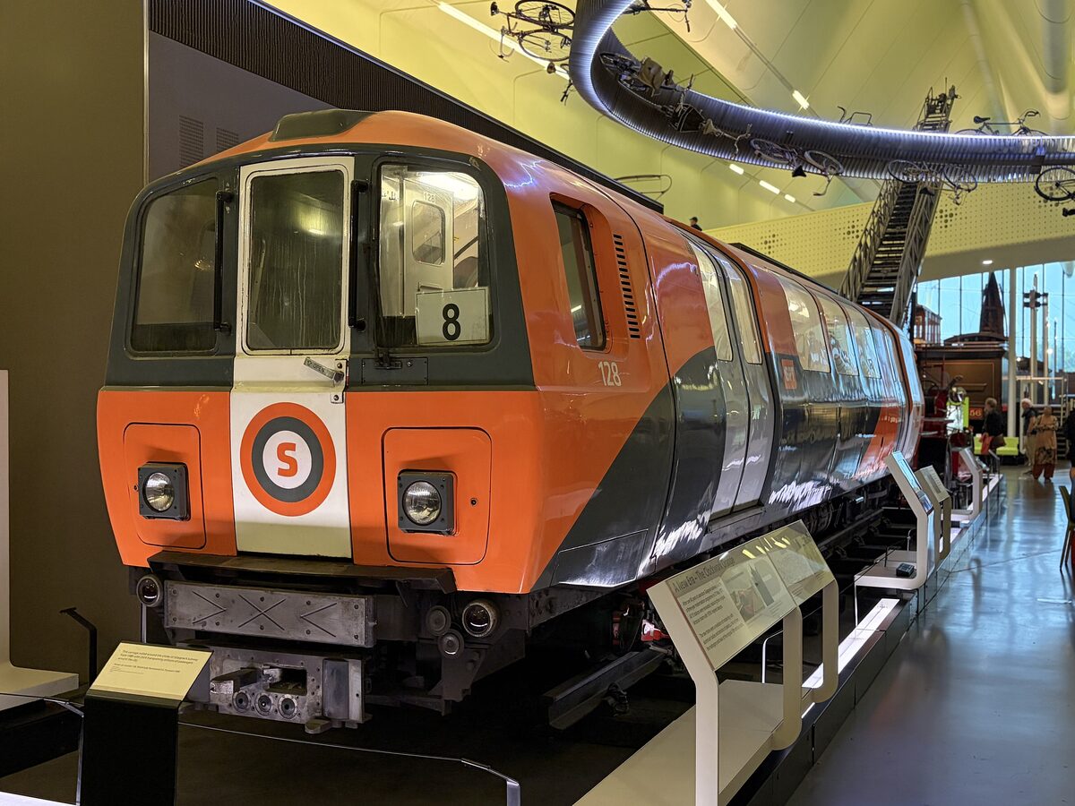 An orange Glasgow Subway carriage on display in the Riverside Museum, with bicycles hanging from the ceiling above