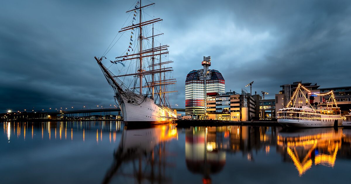 The four-masted barque Viking and the red and white Lipstick tower lit up at dusk, reflected in the calm water of Gothenburg's harbor