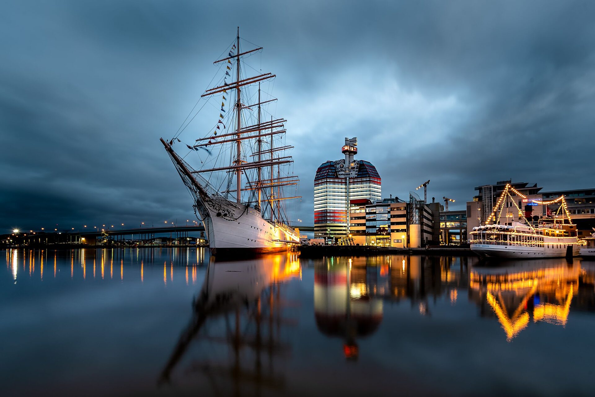 The four-masted barque Viking and the red and white Lipstick tower lit up at dusk, reflected in the calm water of Gothenburg's harbor