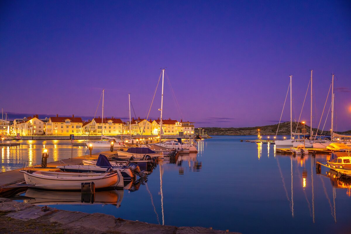 The harbor of Marstrand at dusk, with sailboats and the lit-up wooden houses of the town reflected in the water