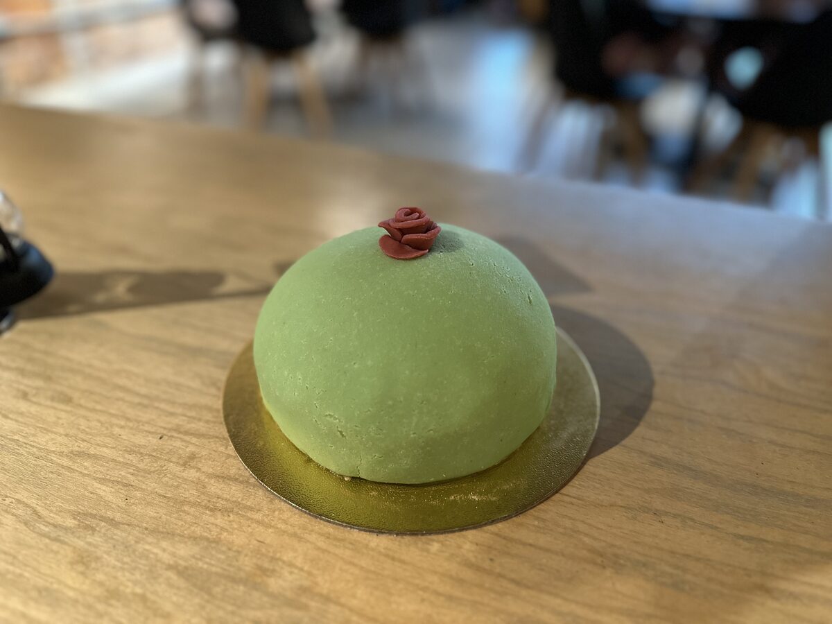 A small princess cake covered in green marzipan with a pink rose on top