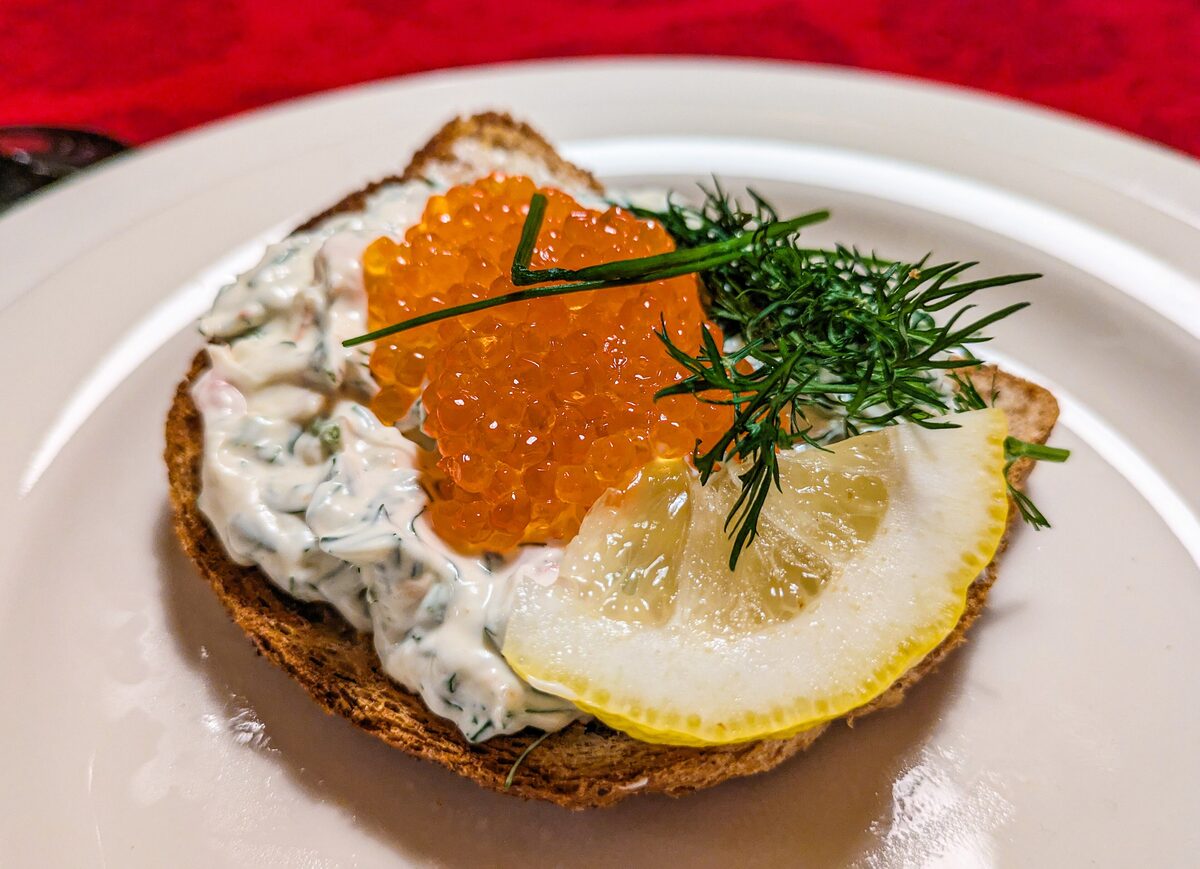 Toast Skagen on a plate: shrimp in mayonnaise and dill on toast, topped with orange roe and a lemon slice