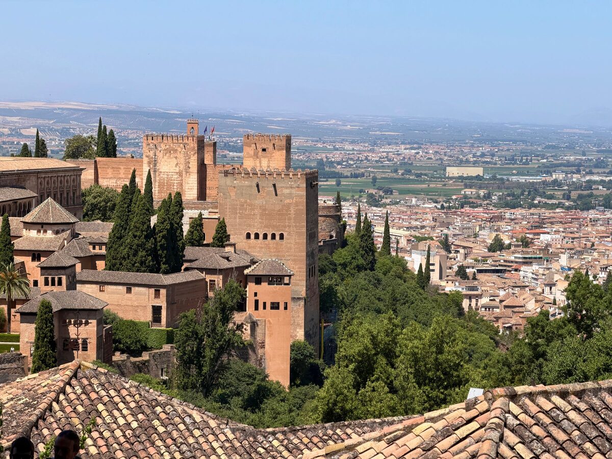 The square towers and walls of the Alcazaba among cypress trees, with the rooftops of Granada and the plain stretching beyond