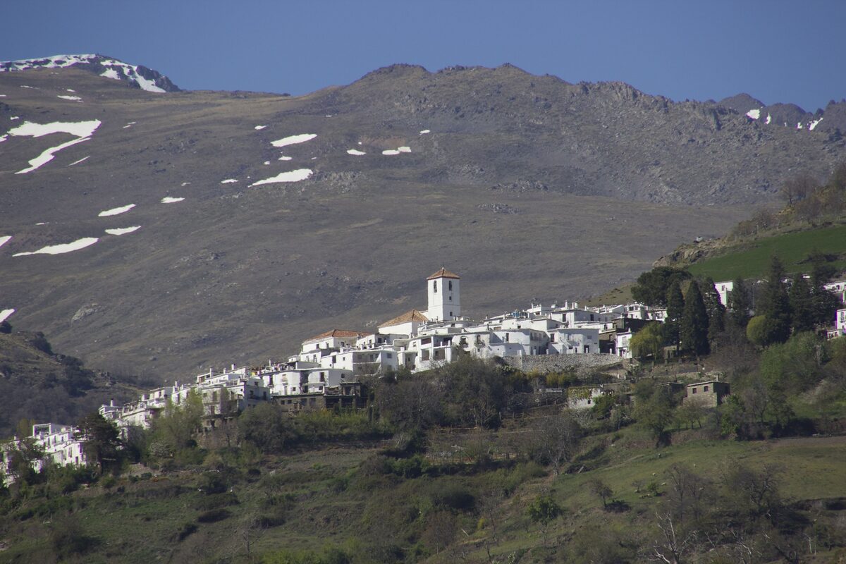 The white village of Capileira on a green hillside, with the bare, snow-streaked slopes of the Sierra Nevada rising behind