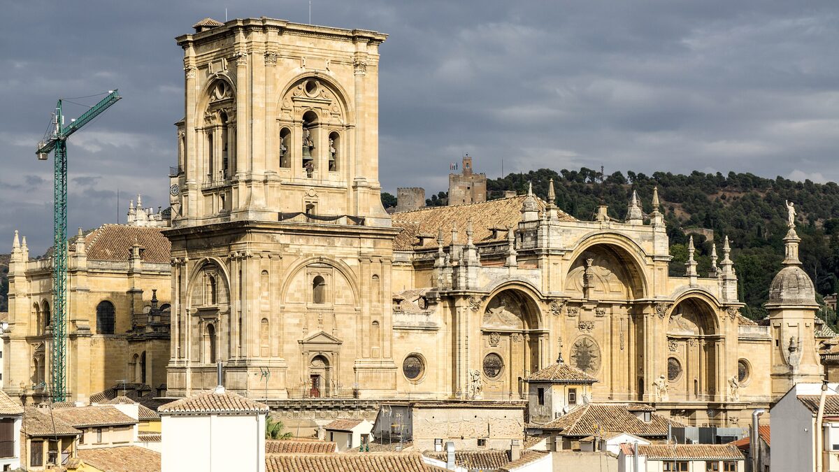 Granada Cathedral rising above the rooftops, with its bell tower and Renaissance facade under a cloudy sky