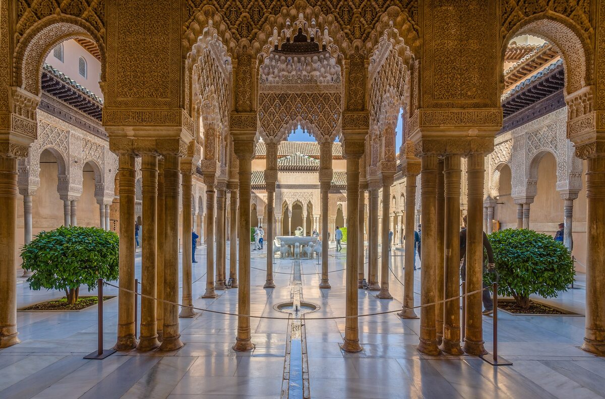 The Court of the Lions seen through slender marble columns and carved arches, with the lion fountain in the middle
