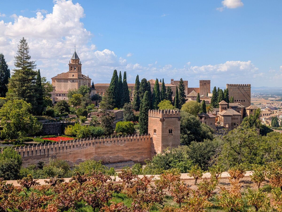 The gardens and walls of the Alhambra seen from above, with cypresses, flower beds and a red-tiled tower