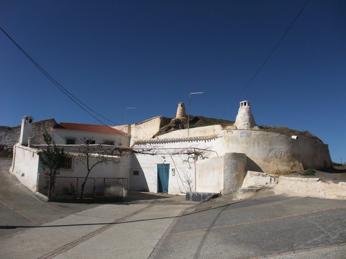 Whitewashed cave houses built into the hillside in Guadix, with white chimneys poking up from the earth above
