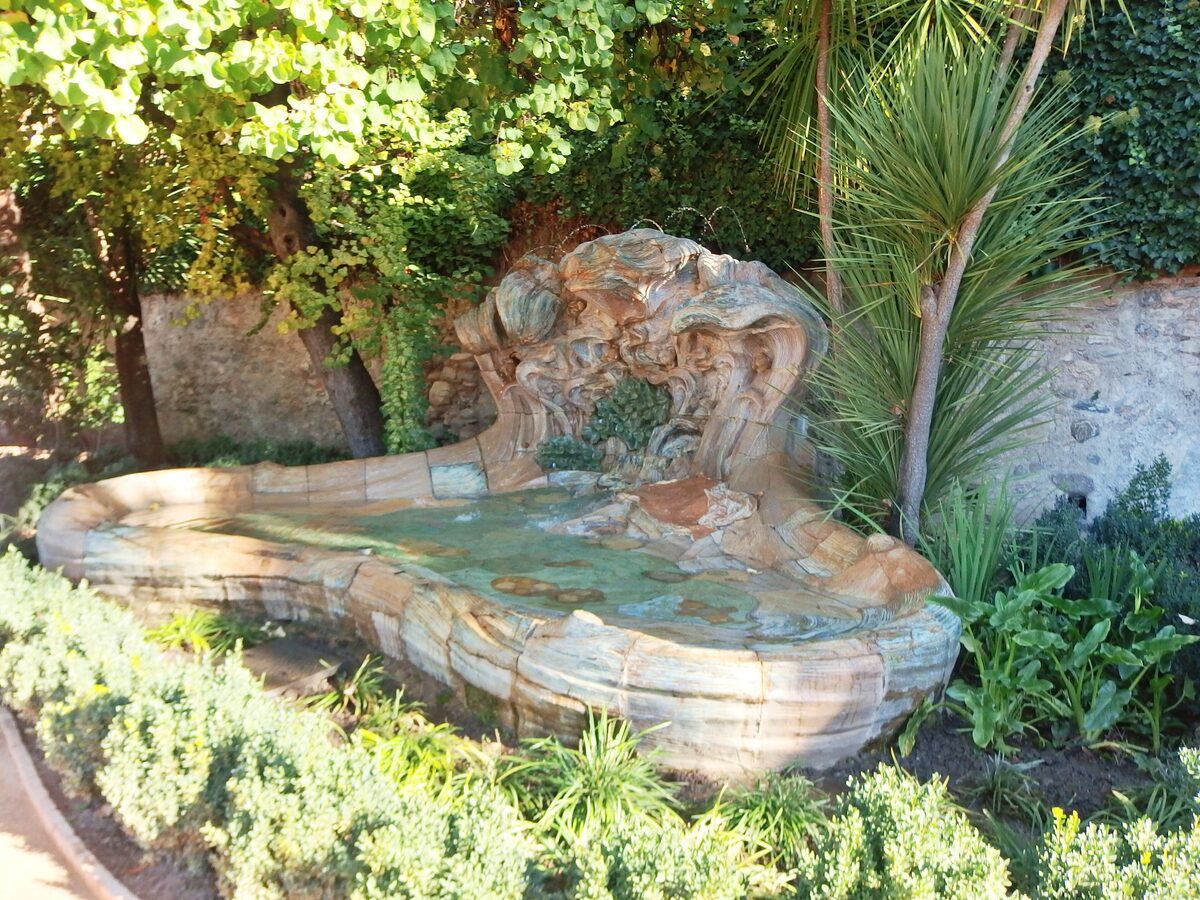 An ornate shell-shaped fountain surrounded by palms and plants in the gardens of the Carmen de los Mártires