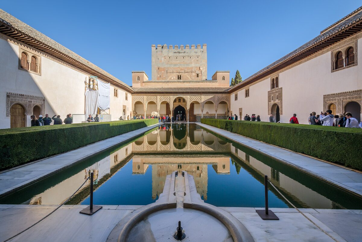 The Court of the Myrtles in the Alhambra, a long pool lined with myrtle hedges reflecting the arcade and the Comares Tower