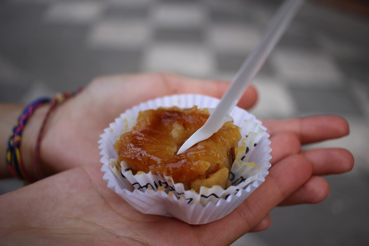 A small pionono pastry in a paper case, with a caramelized top, held in the palm of a hand