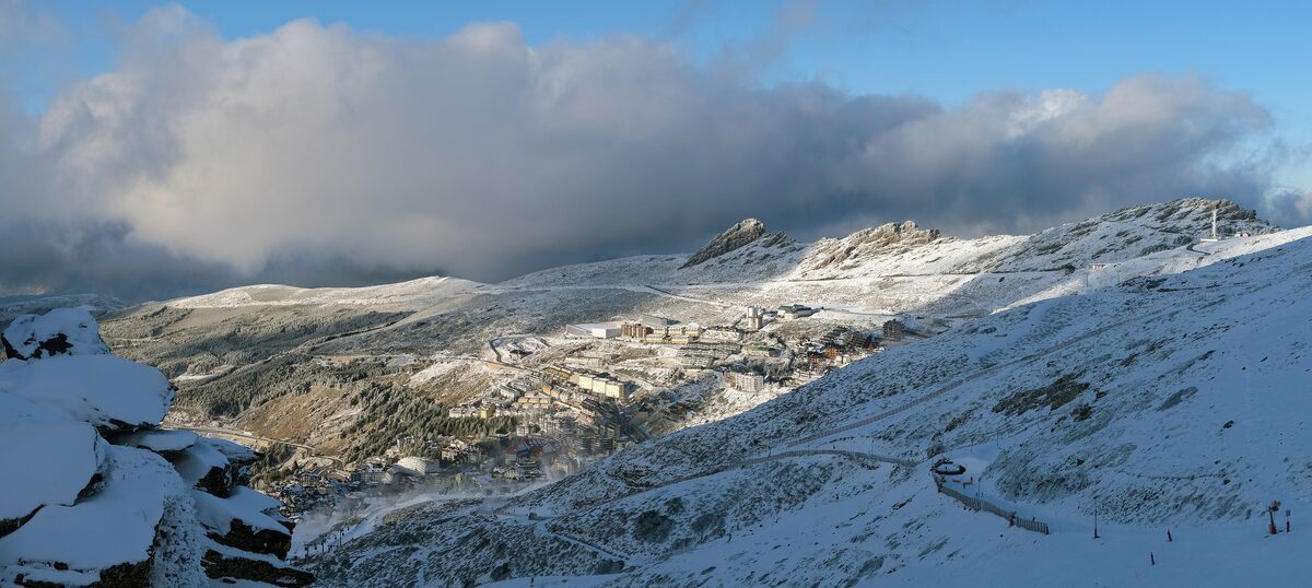 Snow-covered slopes and peaks of the Sierra Nevada under clouds, with a road winding up the mountain