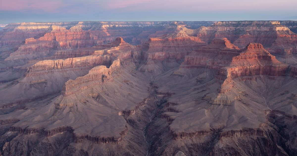 Pink dawn light over layered red canyon ridges seen from Pima Point