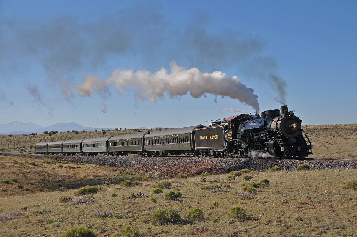 Steam train pulling green coaches across open grassland toward the canyon