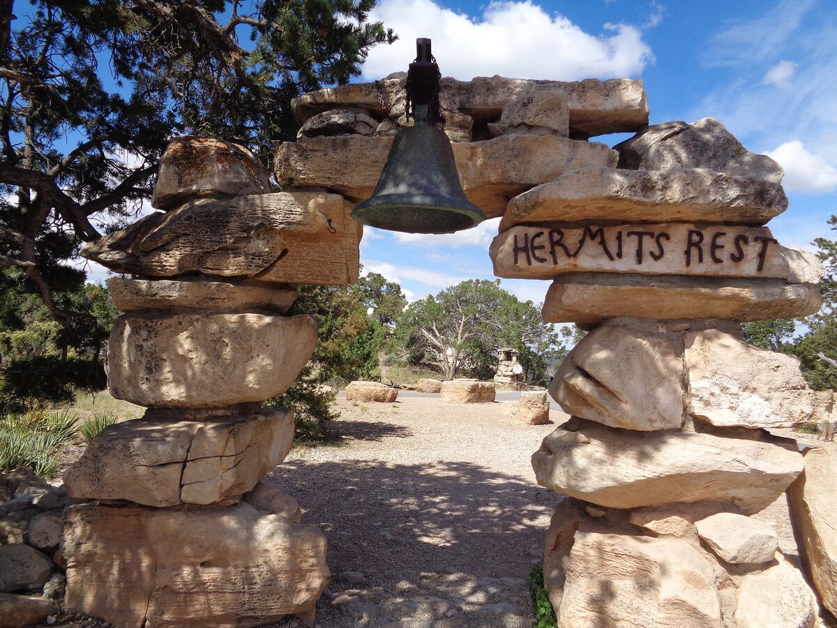 A stone arch with a hanging mission bell and the Hermits Rest sign