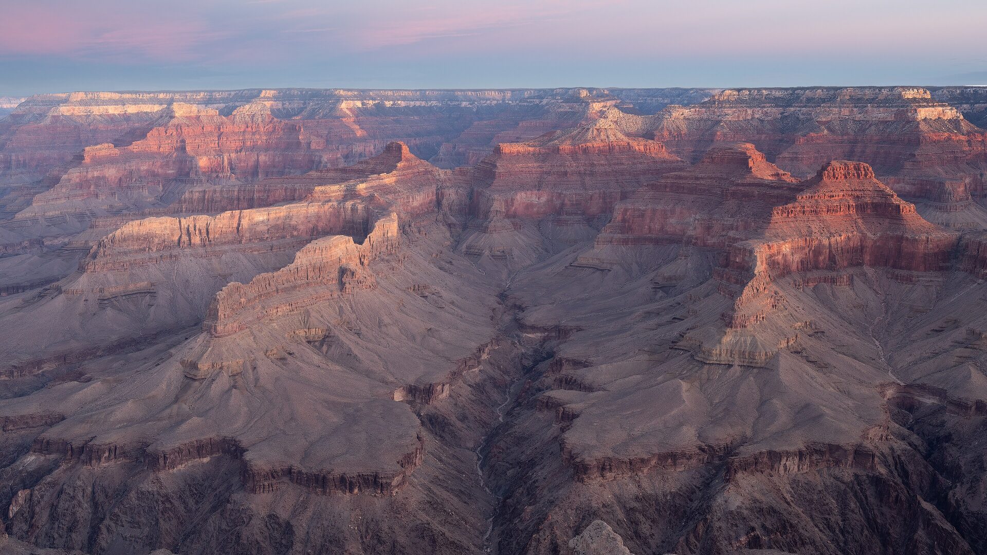 Pink dawn light over layered red canyon ridges seen from Pima Point