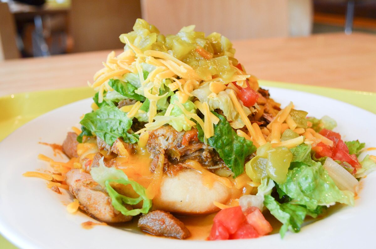 Fry bread piled with lettuce, tomato, green chile, cheese and meat