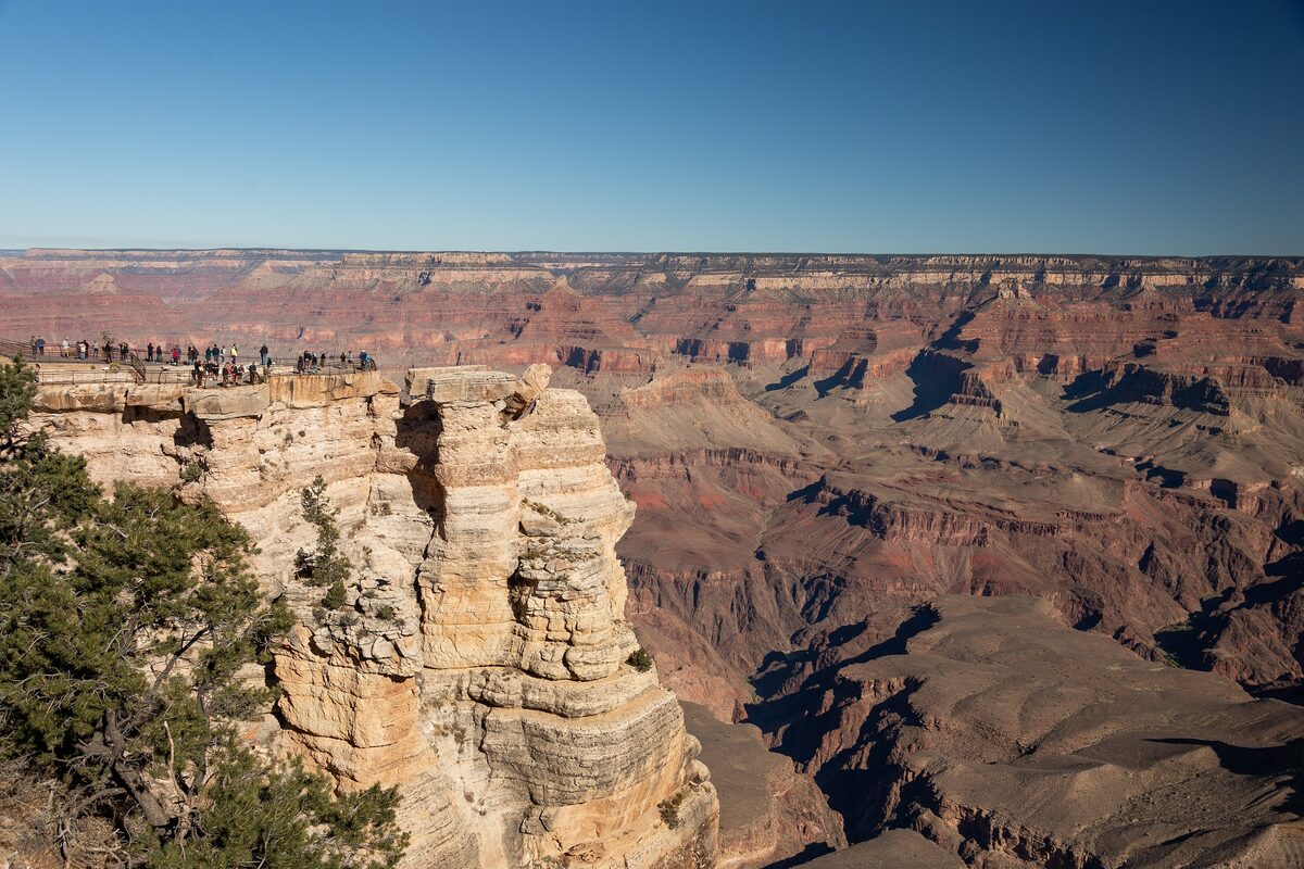 Visitors on a rock overlook above the canyon on a clear day