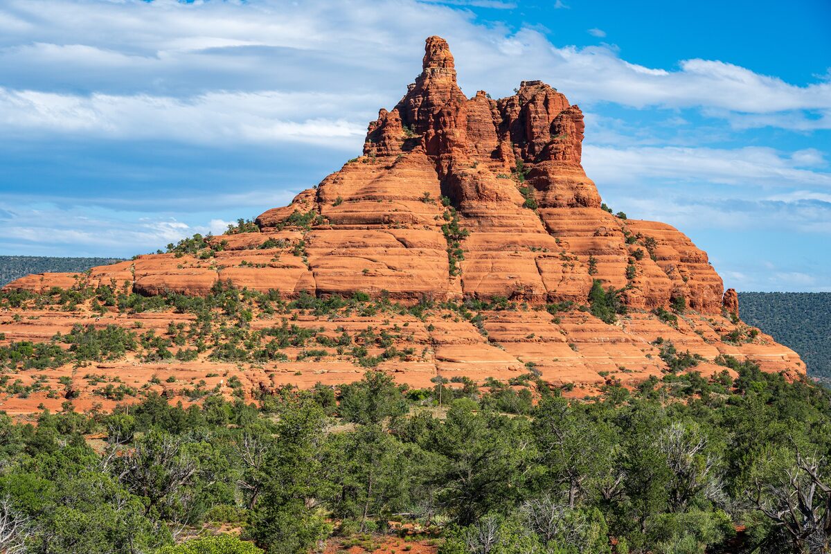 Bell Rock rising above green juniper under a blue sky with clouds