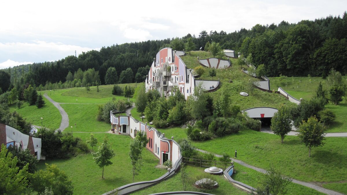 Grass-roofed spa buildings with colorful facades designed by Hundertwasser at Bad Blumau, in green hills