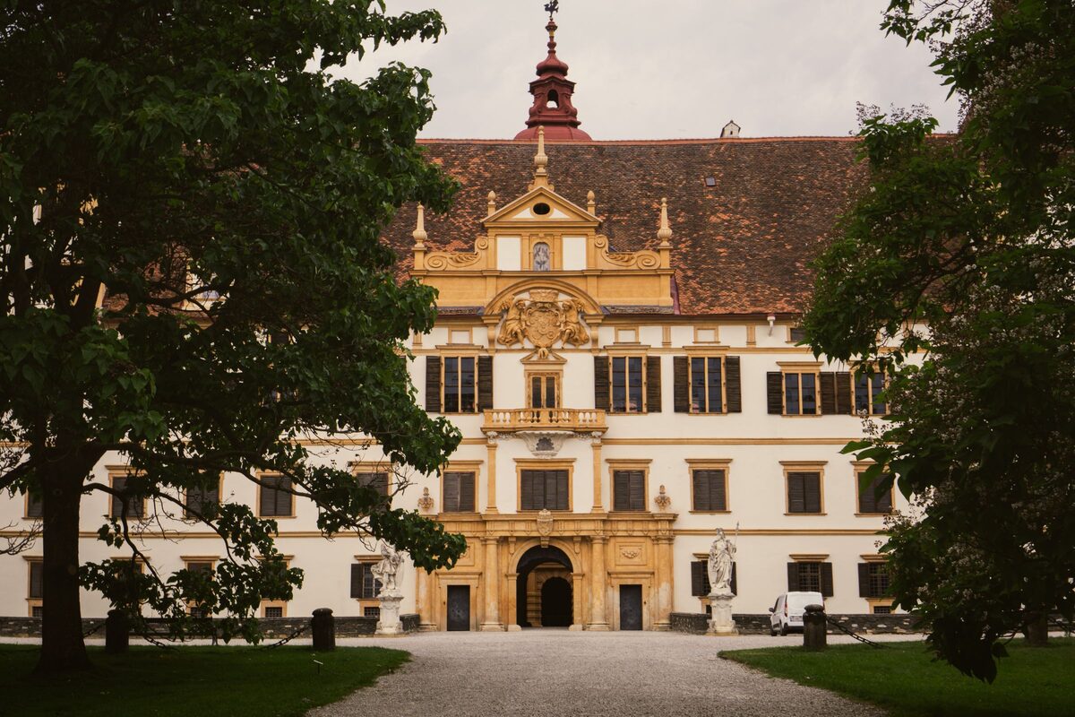 The ornate main portal and facade of Schloss Eggenberg framed by trees