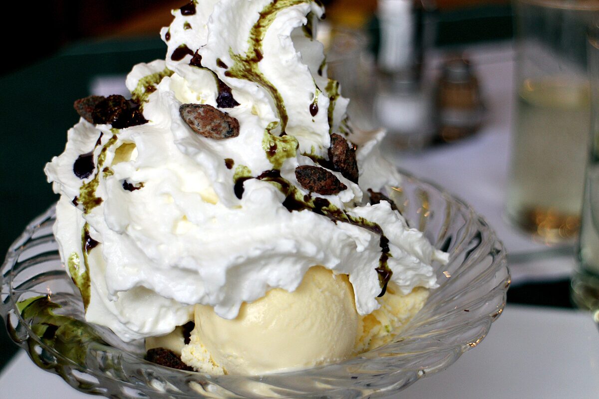 Scoops of vanilla ice cream with whipped cream and dark green pumpkin seed oil drizzled on top
