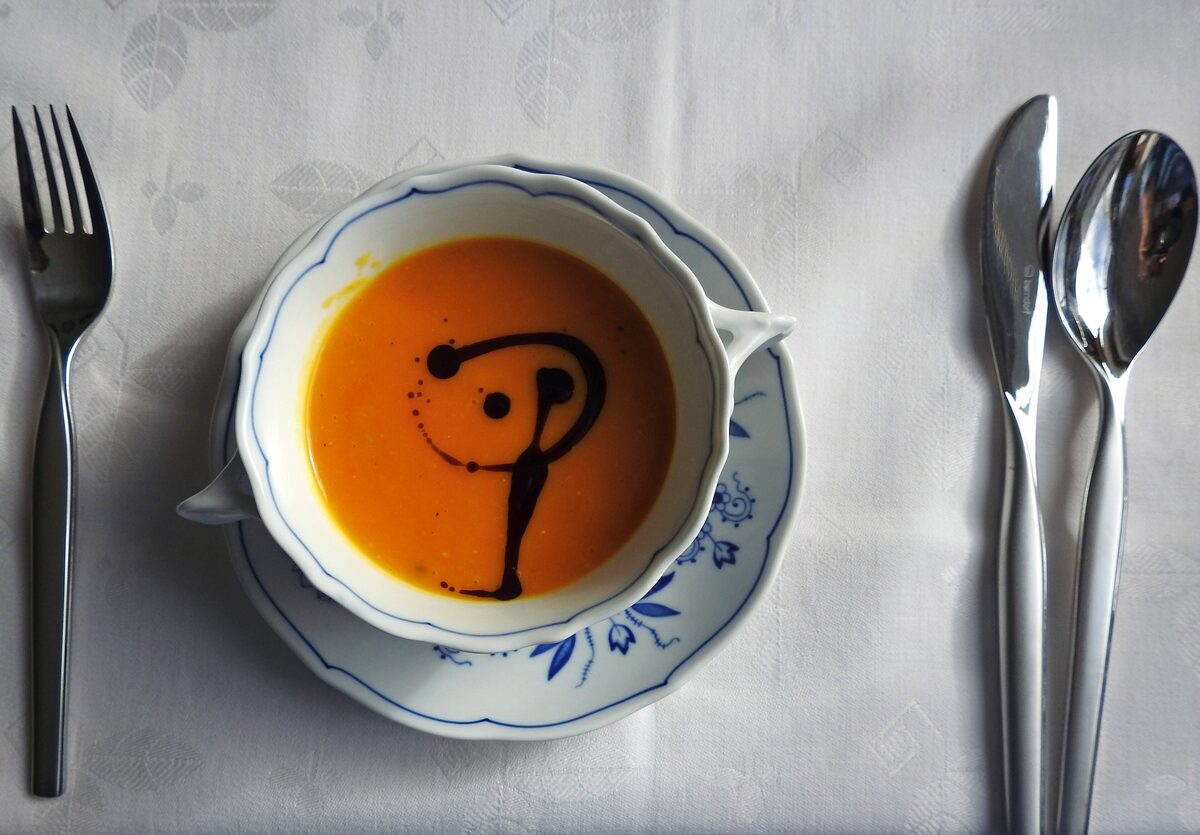 Pumpkin soup in a white bowl with a swirl of dark green pumpkin seed oil