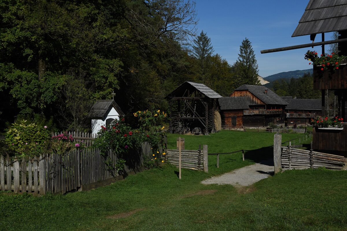 Old wooden farm buildings and a fenced garden in a green valley at the Austrian Open-Air Museum in Stübing