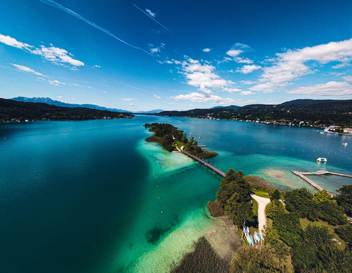 Aerial view of the turquoise Wörthersee with a wooded peninsula and its pier