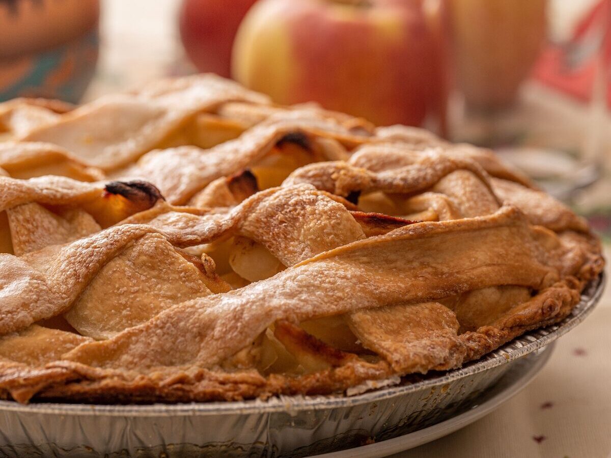 A lattice-topped apple pie with fresh apples behind it