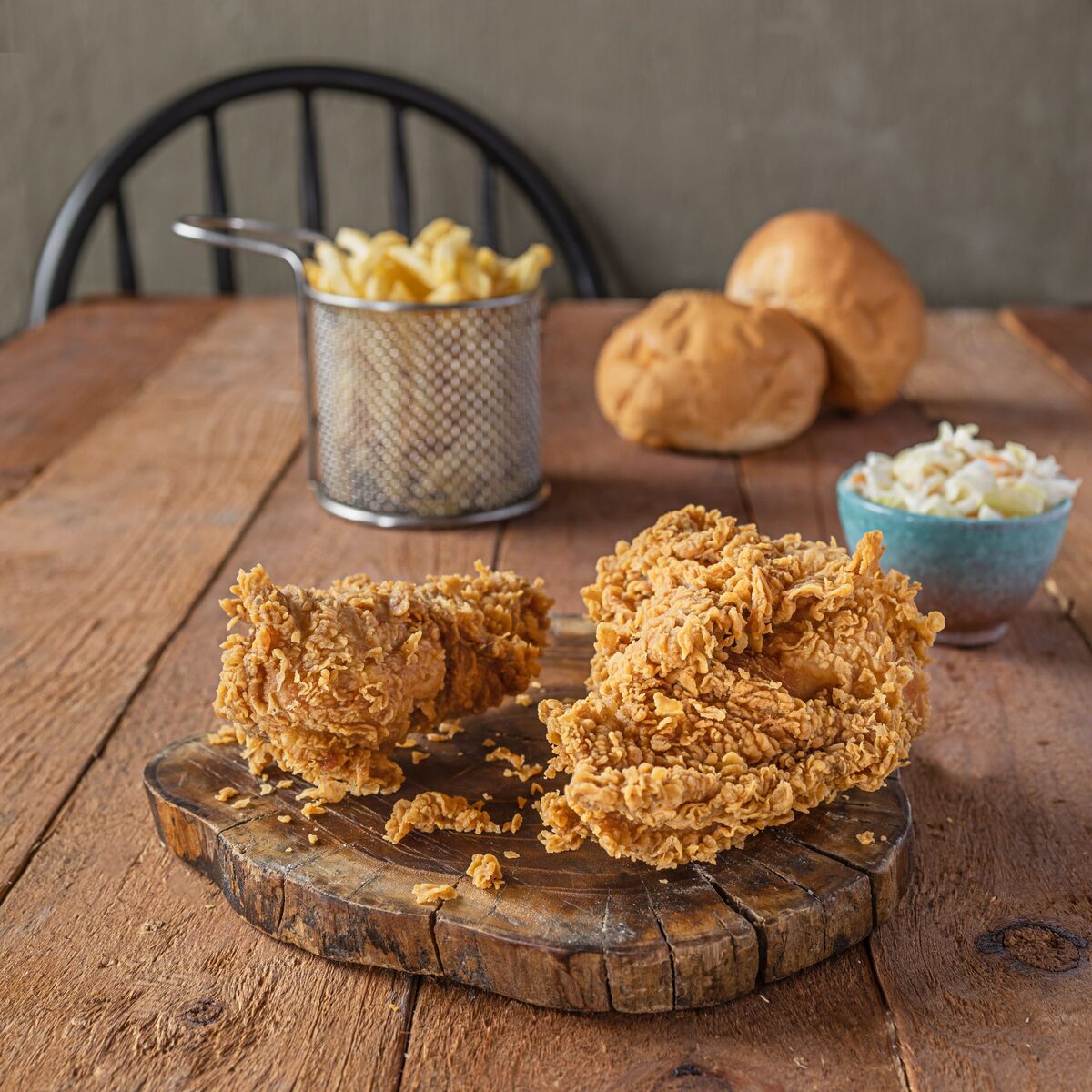 Crispy fried chicken with rolls, coleslaw and fries on a wooden board