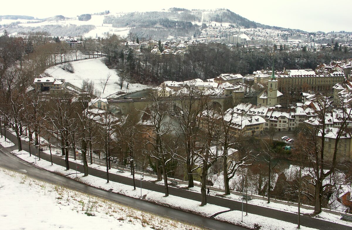 Bern in winter, with snow on the rooftops and bare trees above the river