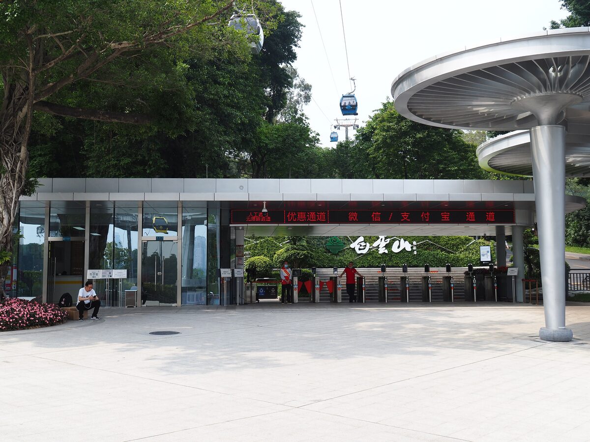 Gondolas of the Baiyun Mountain cable car above the trees beside the station and entrance gates