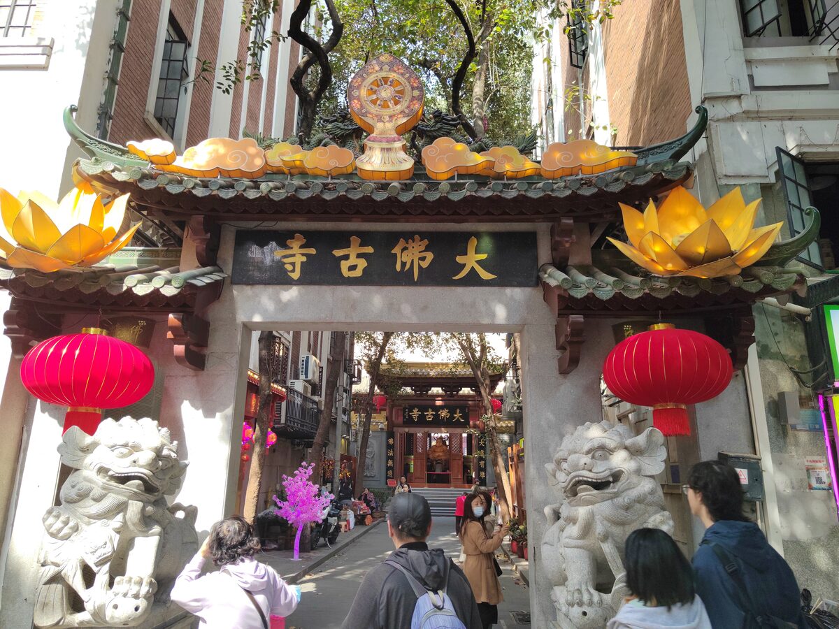 Visitors at the stone-lion gateway to Dafo Temple, with red lanterns and the temple hall down the lane