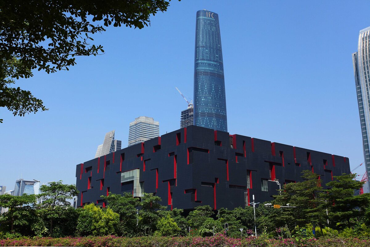 The black boxy facade of the Guangdong Museum with red slits, with a glass skyscraper rising behind it