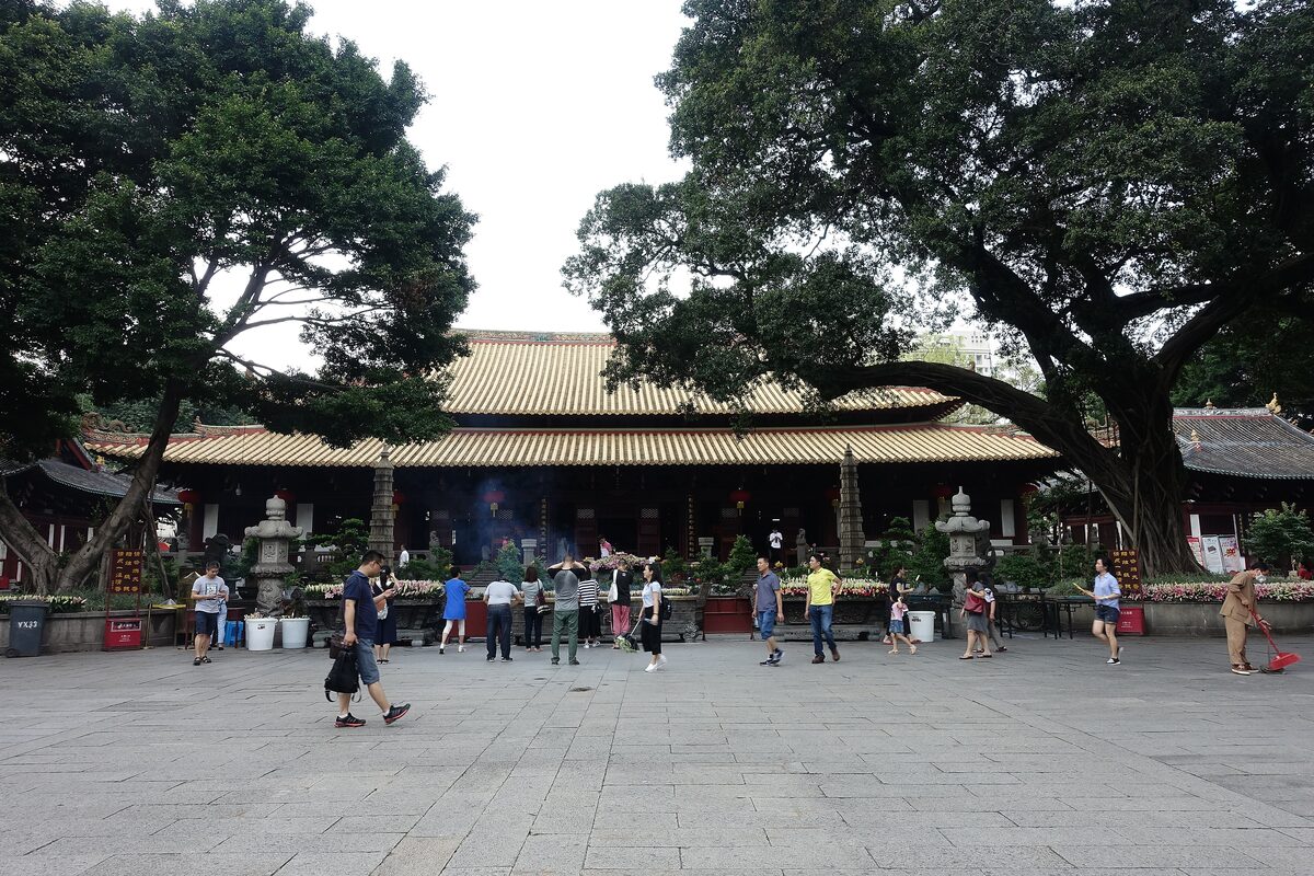 Visitors in the courtyard in front of the Mahavira Hall at Guangxiao Temple, shaded by old banyan trees