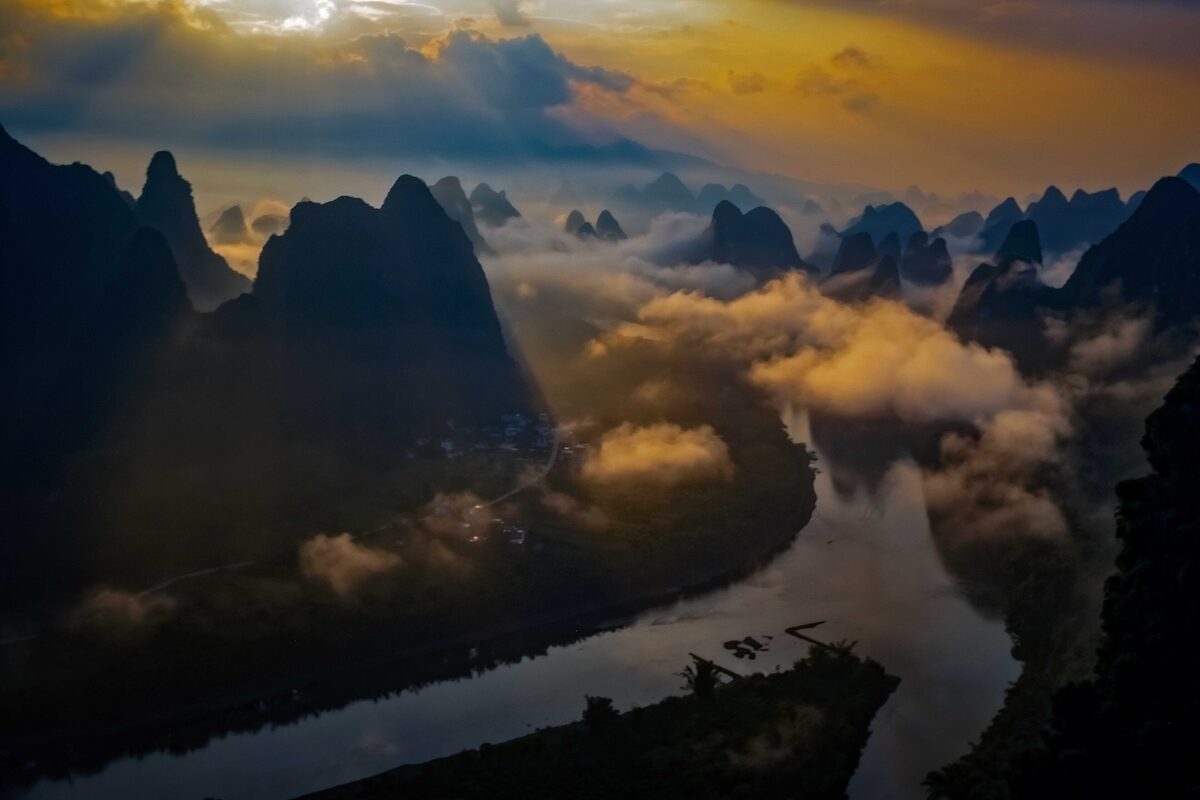 The Li River winding between limestone karst peaks at sunrise, with low cloud and a golden sky