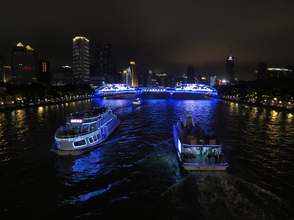 Two lit-up sightseeing boats on the Pearl River at night with a blue-lit bridge and the city skyline behind