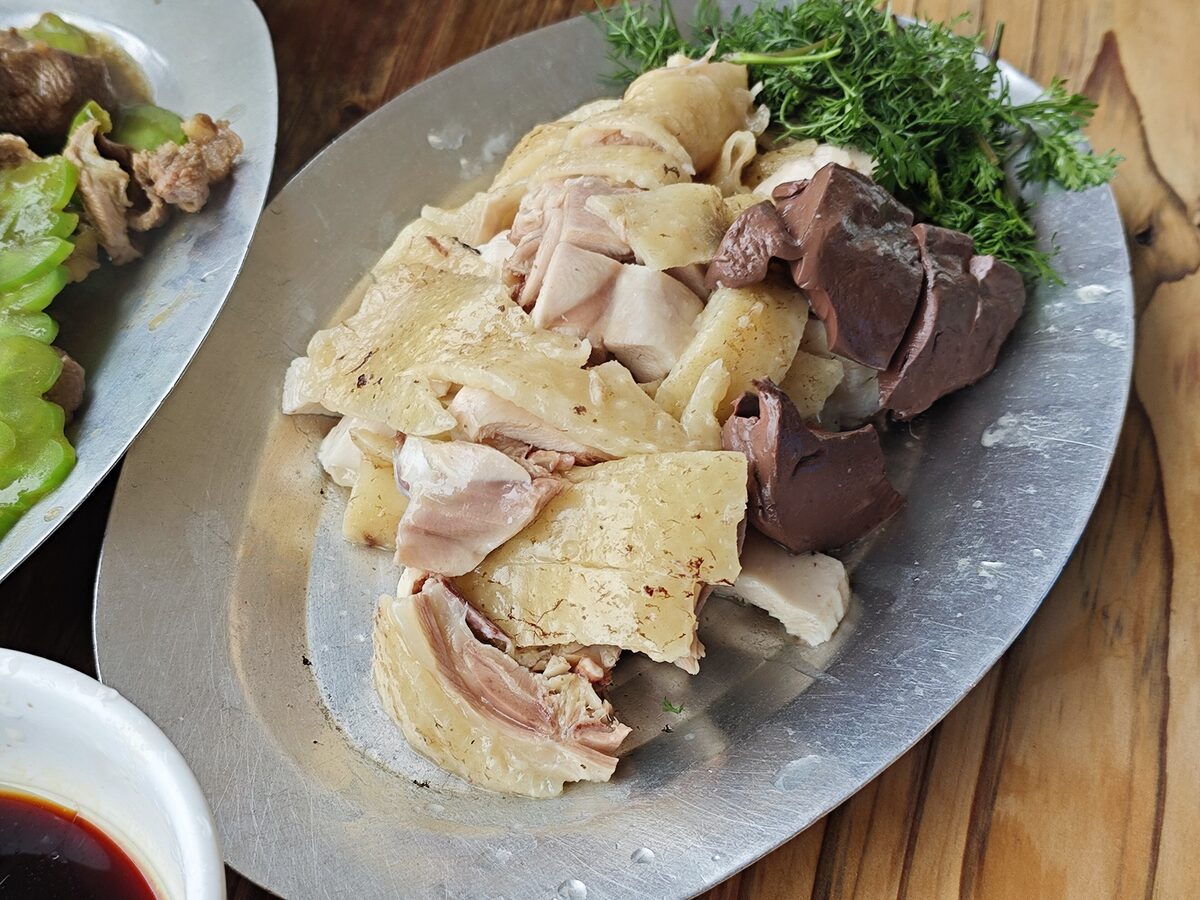 A platter of sliced white cut chicken with herbs and a dish of dipping sauce