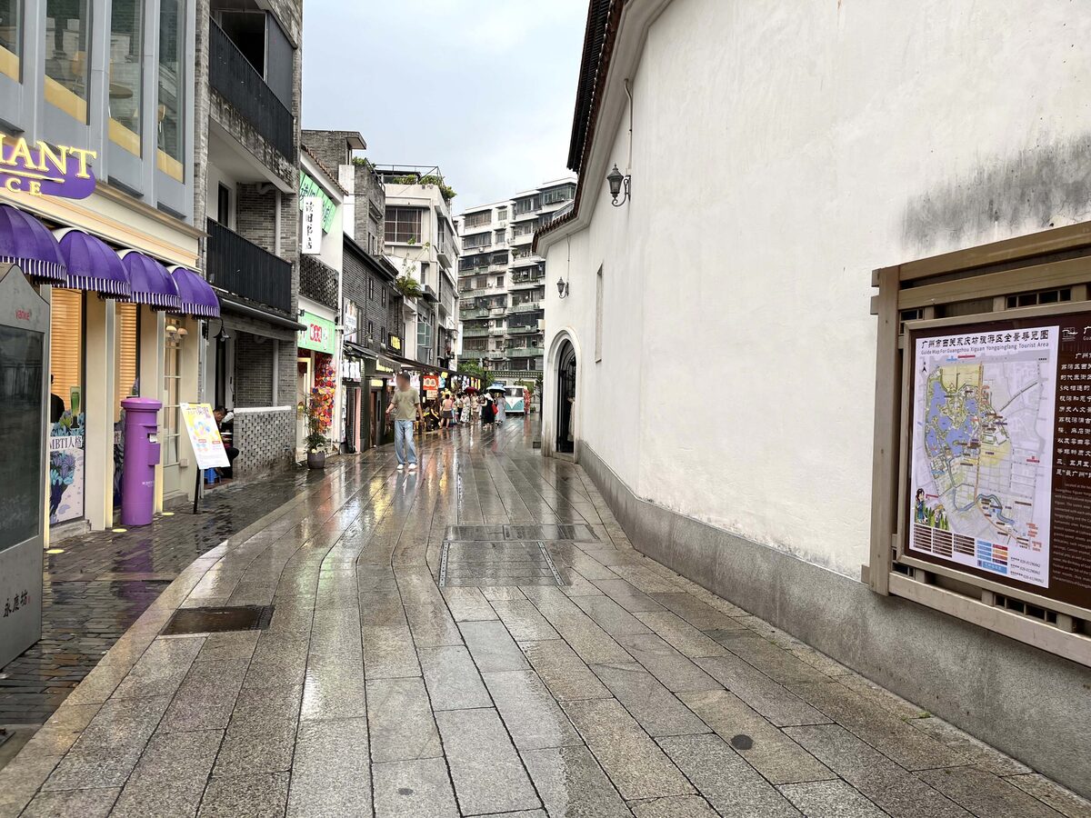 A narrow paved lane in Yongqing Fang between old brick buildings and a white wall, wet after rain