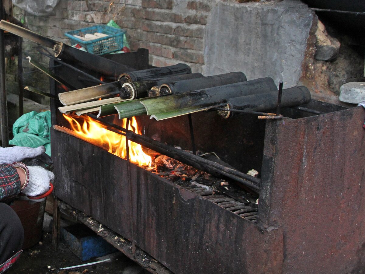 Bamboo tubes of rice cooking over an open fire on a metal grill in Ping'an village