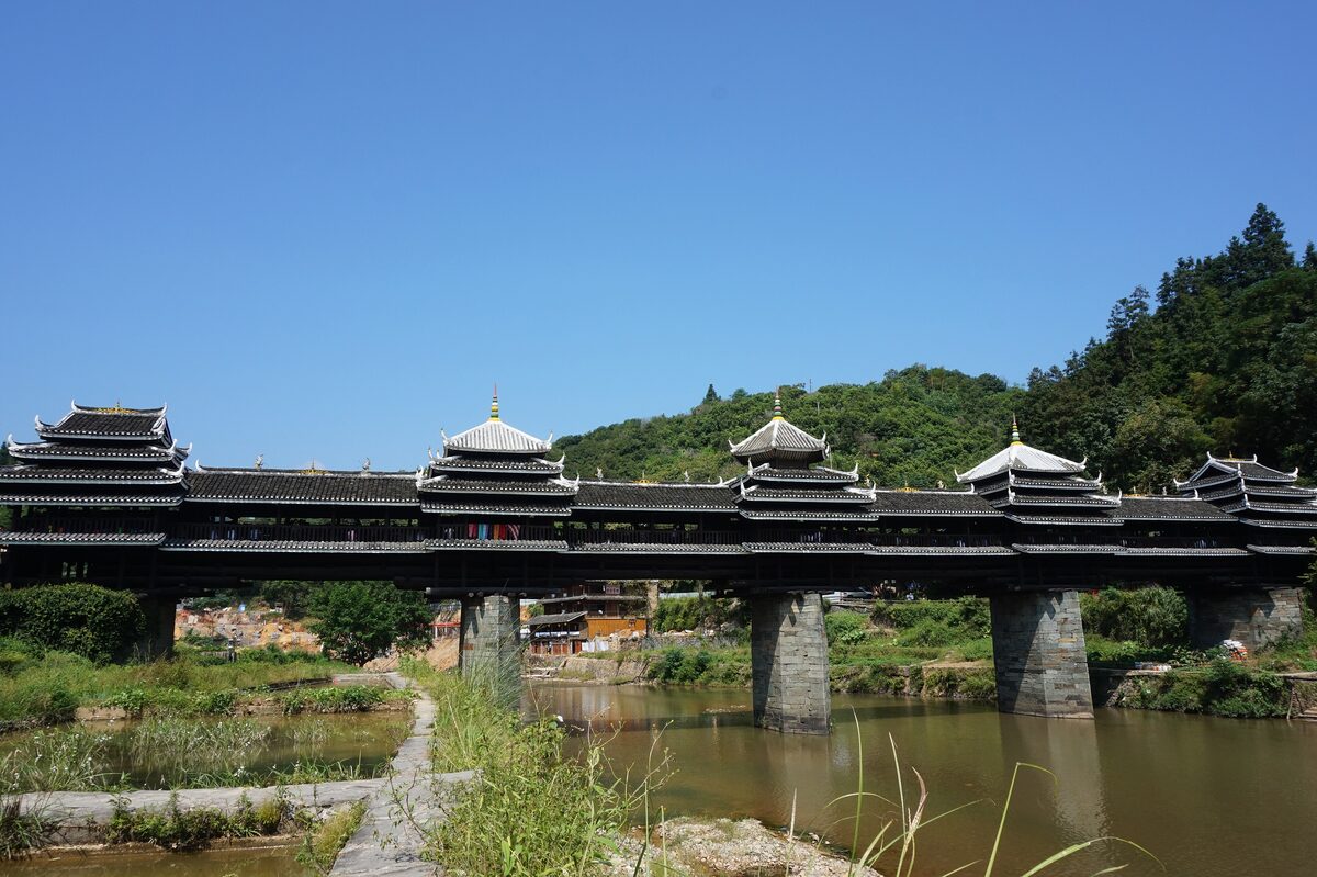 The covered wooden Chengyang Wind and Rain Bridge with its tiered pavilions over a river on a sunny day