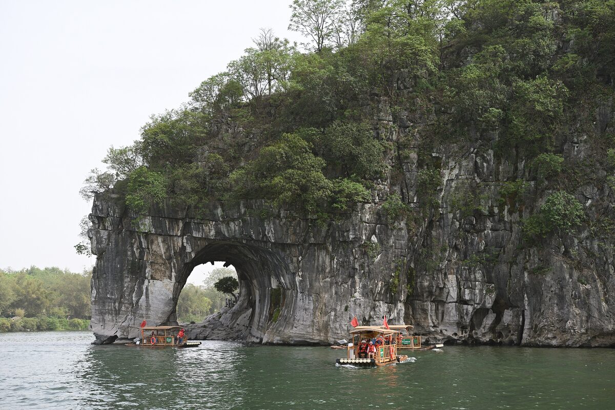 Elephant Trunk Hill in Guilin, a wooded limestone hill with a round arch at the water's edge and bamboo rafts in front