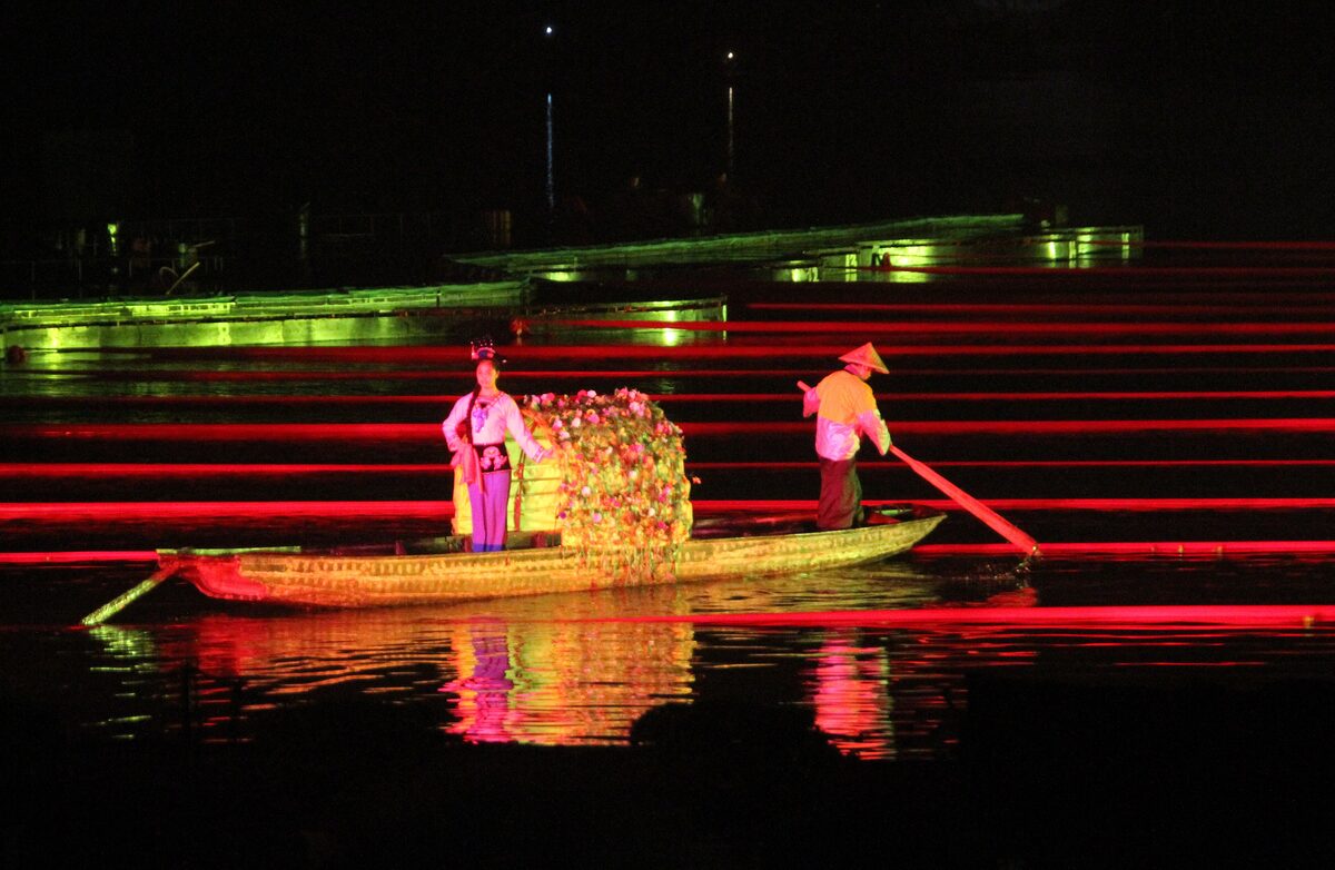 Performers on a decorated boat gliding over the red-lit water of the Impression Liu Sanjie night show