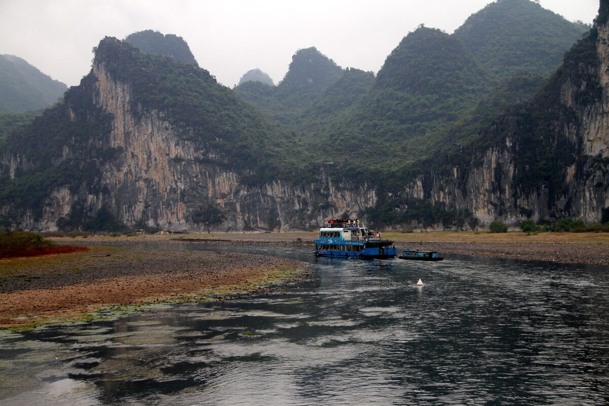 A cruise boat on the Li River below steep limestone cliffs and karst peaks