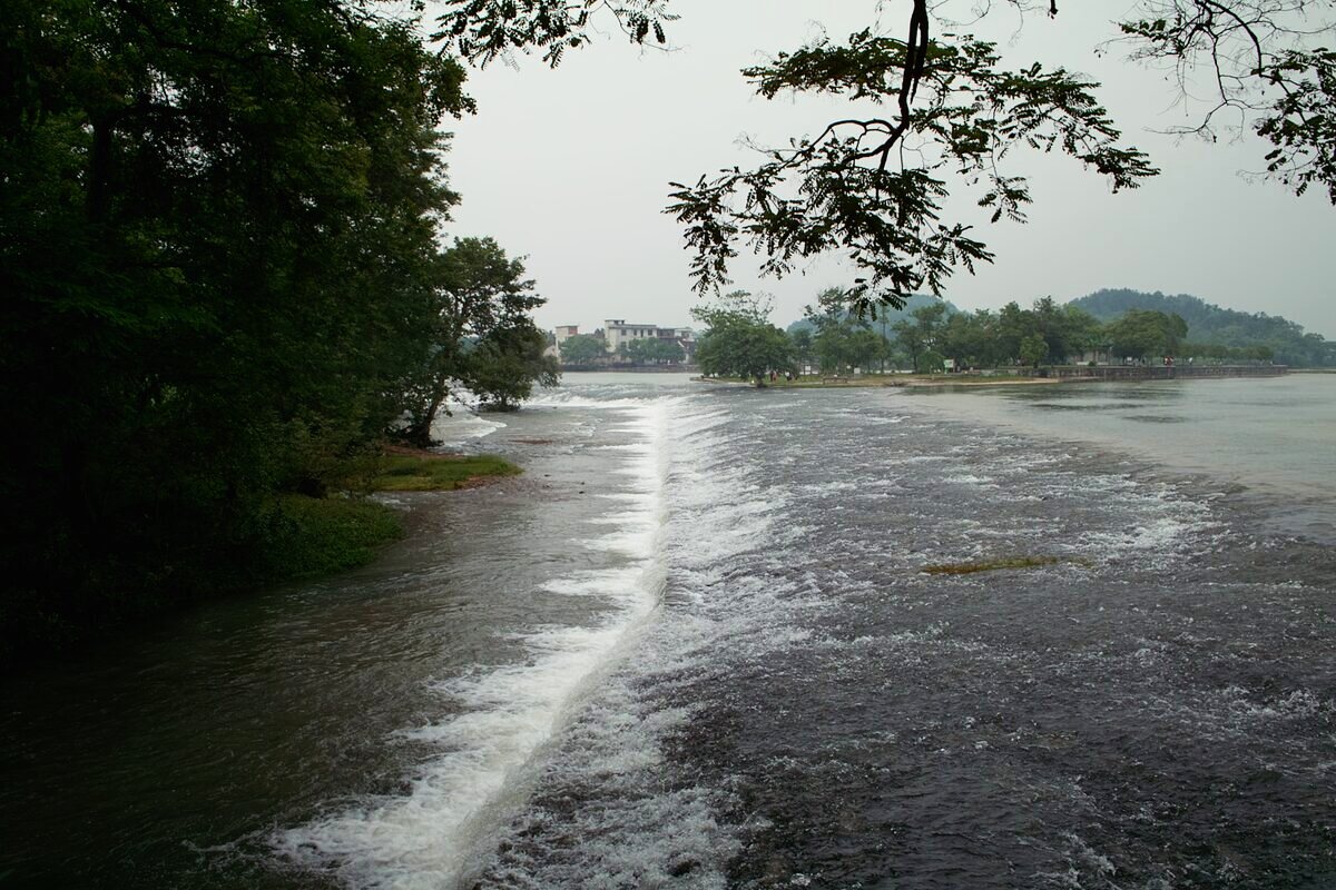 Water spilling over a low weir on the Lingqu Canal in Xing'an County under an overcast sky